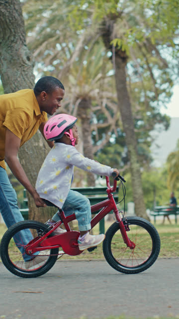 Encouraging Confidence and Growth: African American Father Guides His Daughter's Bike Riding Development at the Park