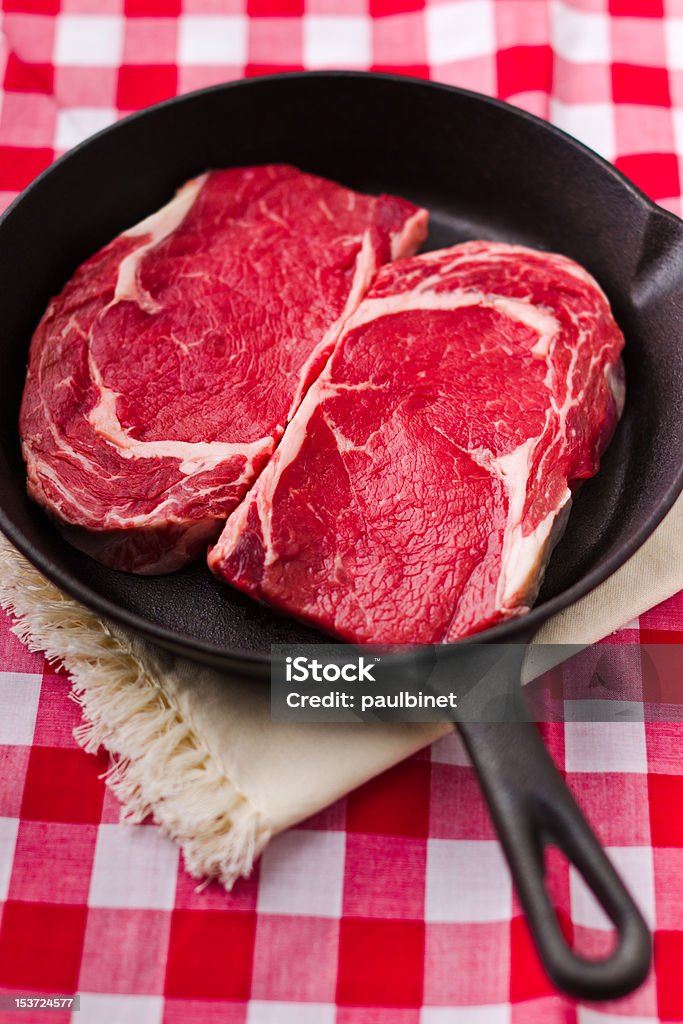 raw beef meat Two beautiful pieces of raw beef meat in a black iron frying pan. Shallow depth of field and red background. Beef Stock Photo