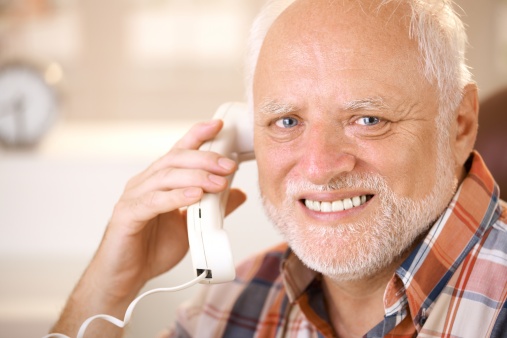 Closeup portrait of smiling senior man using landline phone, looking at camera...