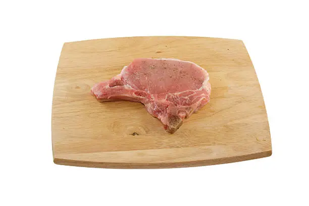 fresh porkchop lighly seasoned with salt and pepper on a woodgrain cutting board on white