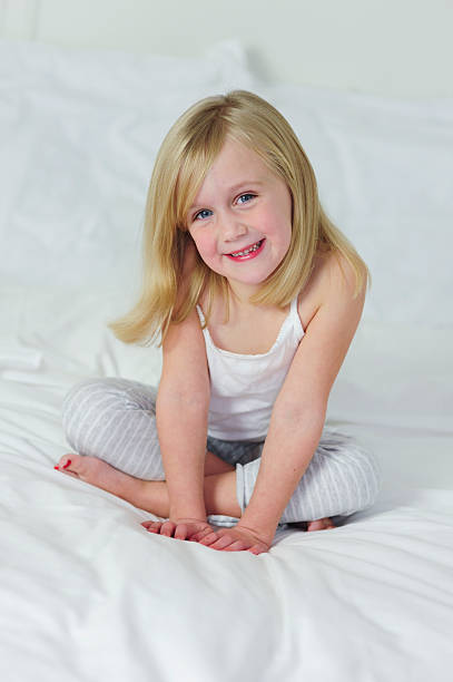 Little girl sitting indian style on a white bed. stock photo