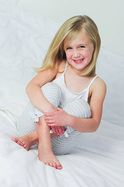 Little girl hugging knees on a bed stock photo