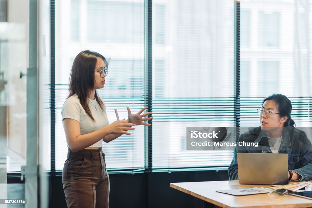 Asian chinese beautiful young woman giving presentation in front with team at design studio side view of young woman standing and having discussion with team Explaining Stock Photo