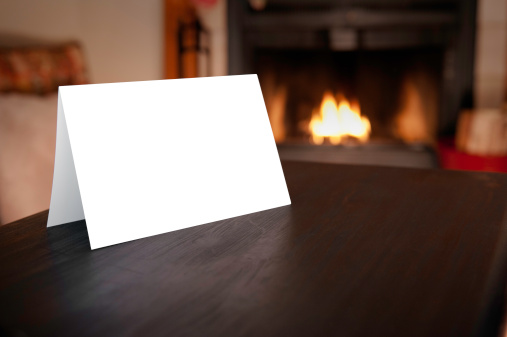 Blank horizontal christmas card folded in front of burning fireplace