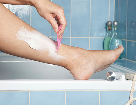 Woman's hands shaving her legs with depilatory cream