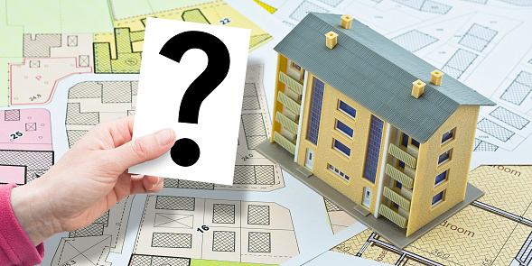 Doubts and uncertainties about buildings - concept with imaginary cadastral map and general urban plan with condominium residential building with and holding a card with question mark