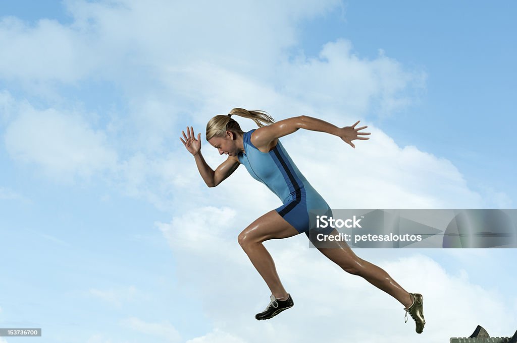 Female sprinter running in front of a blue sky Femaile sprinter leaps from starting block. Blue Stock Photo