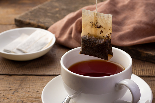 Herbal tea and the teabag in an elegant teacup and saucer on a colourful placemat