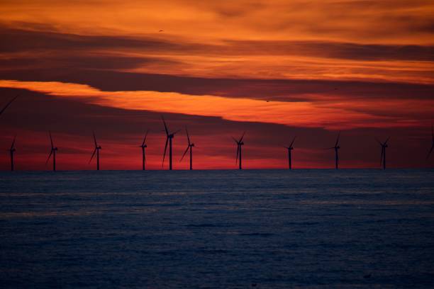 beau ciel orange illuminé par un coucher de soleil doré avec plusieurs éoliennes au premier plan - dramatic sky dusk night sustainable resources photos et images de collection