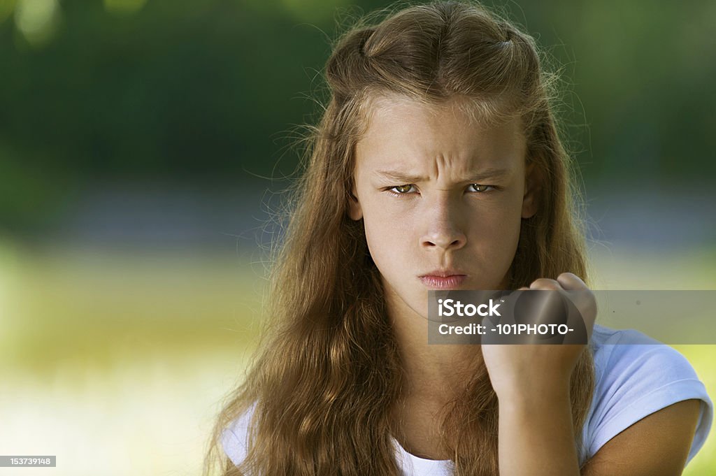 severe teenage girl shakes her fist Beautiful severe teenage girl shakes her fist, against green of summer park. Adult Stock Photo