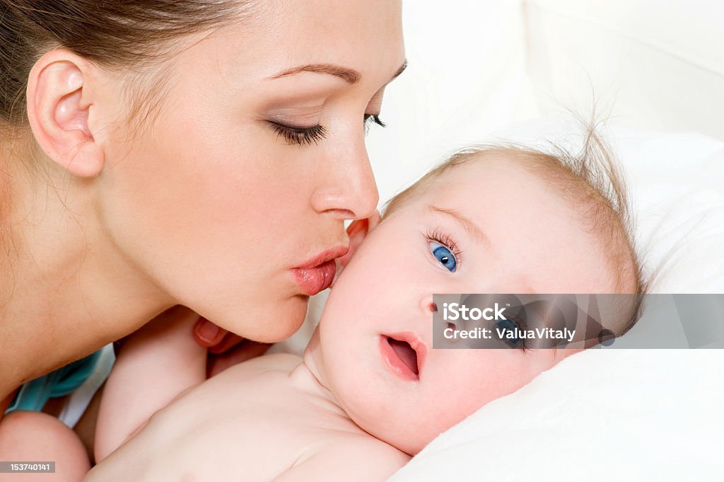 A mother kissing her newborn baby Closeup faces of young happy mother with cute newborn baby Adult Stock Photo