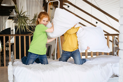 Red-haired children fight with pillows on the bed at home. The children had fun. Good relationship between brother and sister