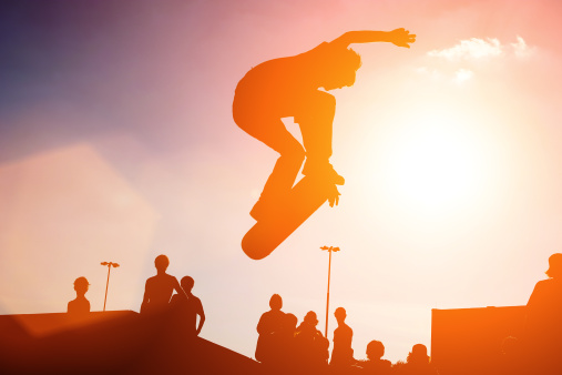Jumping skateboarder silhouette over sunset sky background
