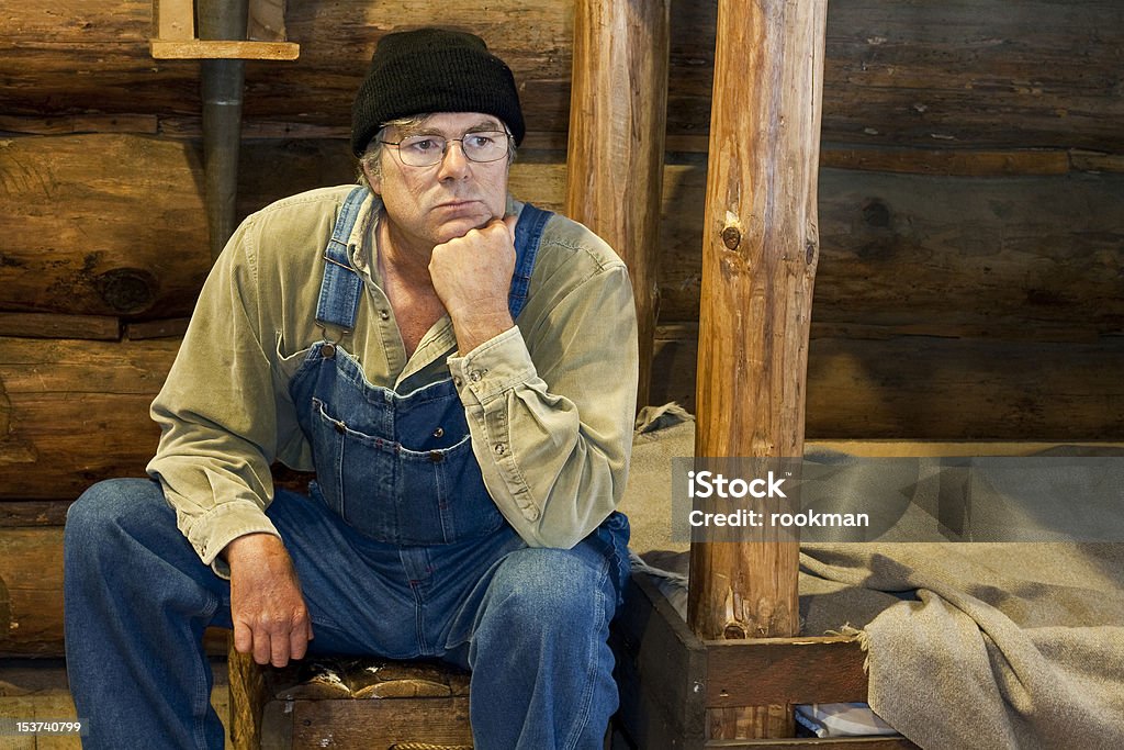 man sitting in his log cabin thinking man in bib overalls sitting in his log cabin thinking about life Adult Stock Photo