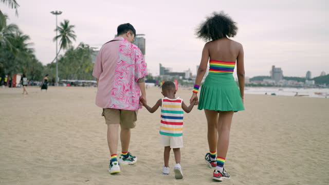 LGBTQ lesbian parents and little son holding hands together and walking on beach, Multiracial family having joyful moment together to support diversity, Happy family having wonderful outdoor activity in summer
