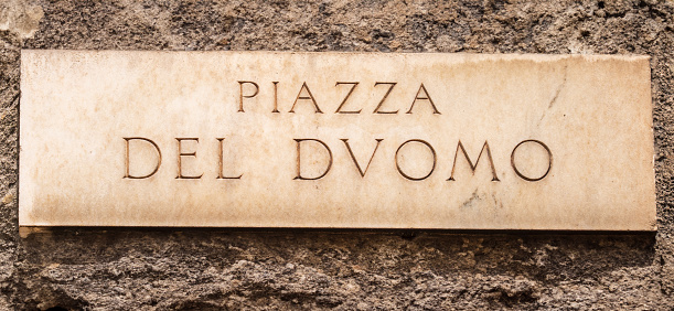 antique marble sign indicating the central Piazza del Duomo in Milan, bearing classical-style characters, affixed to a stone wall