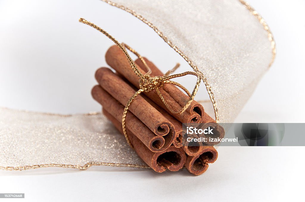 Stack of cinnamon sticks decorated with gold ribbons Stack of cinnamon sticks tied in gold ribbon and decorated with gold Christmas ribbon on white isolating background Brown Stock Photo
