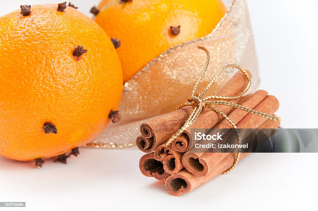 Closeup of two cloves-decorated oranges and cinnamon sticks Close-up of two cloves-decorated oranges and cinnamon sticks in the stack with gold ribbon, gold ribbon in the background, white, isolating background Brown Stock Photo