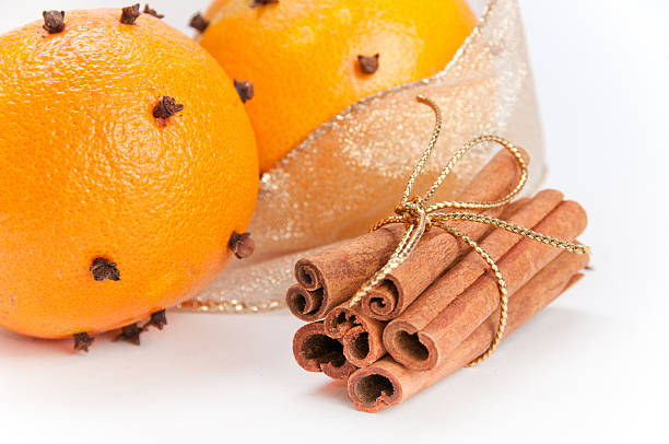 Closeup of two cloves-decorated oranges and cinnamon sticks stock photo
