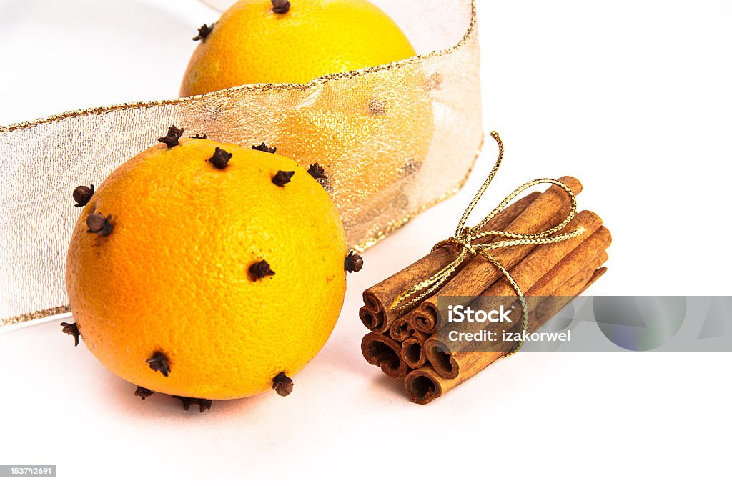 Two cloves-decorated ornages, cinnamon sticks and riboons Two cloves-decorated oranges and cinnamon sticks in the stack with gold ribbon, gold ribbon in the background, white, isolating background Brown Stock Photo