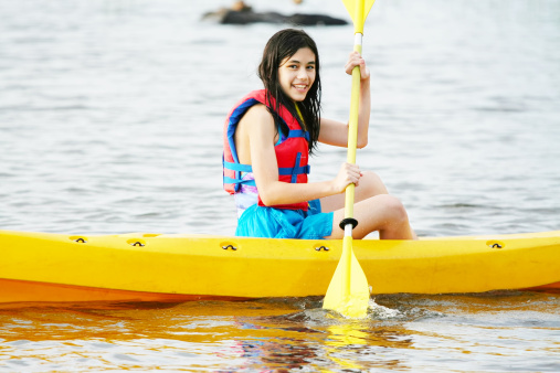 Young teen part Asian girl kayaking in yellow kayak on lake
