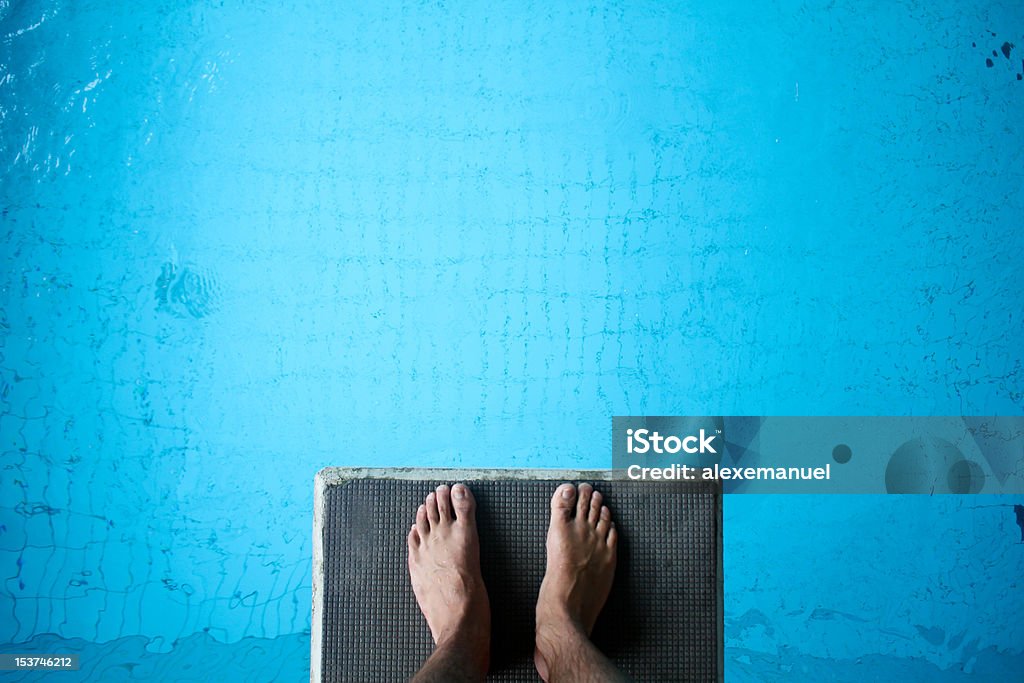 Aerial view of man's feet on diving board on blue man standing on diving platform above pool Diving Into Water Stock Photo