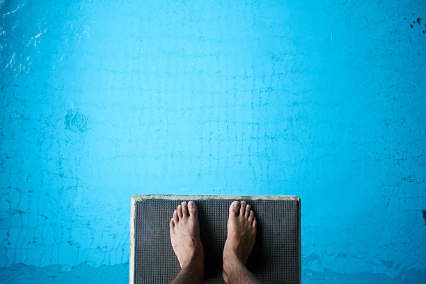 Aerial view of man's feet on diving board on blue man standing on diving platform above pool diving into water stock pictures, royalty-free photos & images