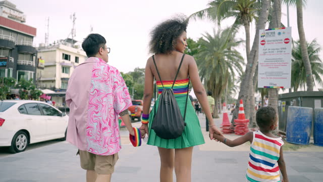 LGBTQ lesbian parents and little son holding hands together and walking on street, Multiracial family spending wonderful outdoor activity near beach in summer, LGBTQ lesbian family supporting child adoption