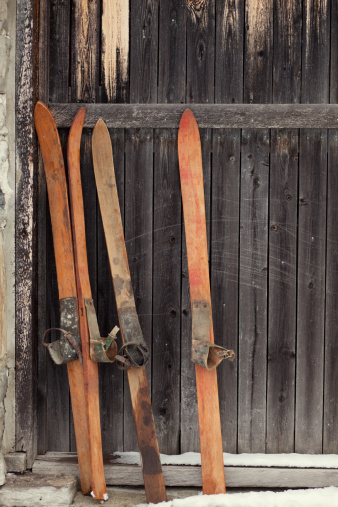 Two sets of antique skis lean against an old barn in winter. Space for copy.