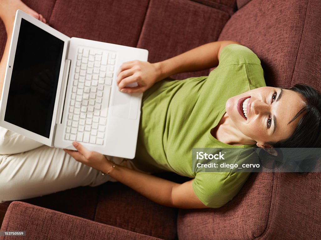 Mujer sonriente en sofá con pc - Foto de stock de 30-34 años libre de derechos