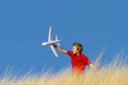 Action shot of young boy flying model airplane against clear blue sky.