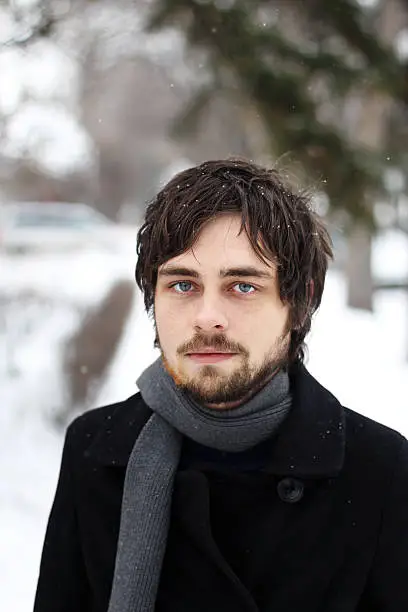Young male portrait dressed in a heavy jacket and scarf on a snowy winter day.