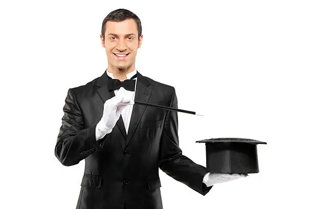 A magician in a black suit holding an empty top hat and magic wand isolated on white background