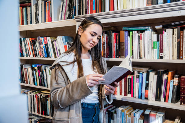 istock Young woman reading a book in the library 1537564663