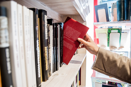 Close-up of a woman picking a book from bookshelf in the library