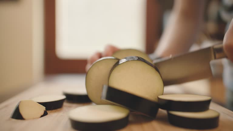 hand cutting aubergine on wooden chopping board