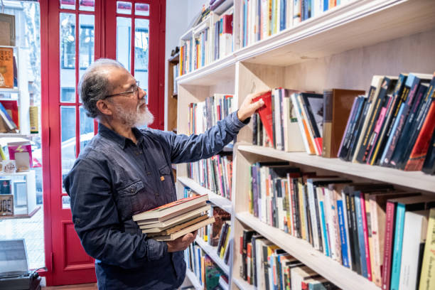 istock Senior man picking up books in the library 1537574223