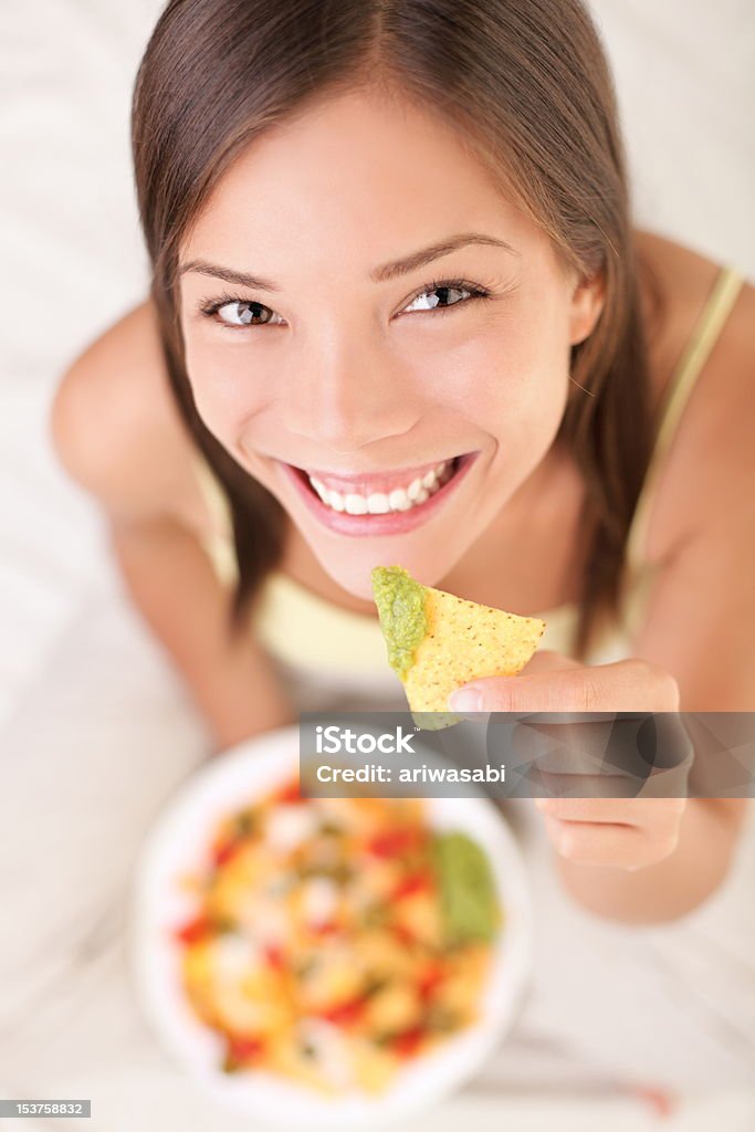 Woman eating nachos Nachos eating woman smiling looking at camera. Beautiful cute girl enjoying snacks in bed - white background. See more: Eating Stock Photo