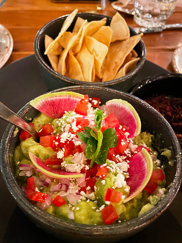 A bowl of freshly made  guacamole , with avocado, tomato red reddish with the side of tortilla chips.