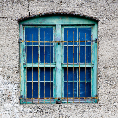 An old green window with rusty bars set in concrete with weathered paint peeling off.
