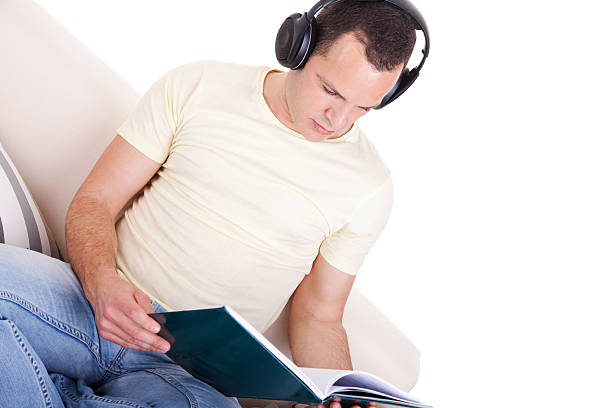 man reading and listening music with headphones on couch stock photo