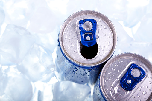 Photo of the top two opened chilled cans of energy drink in ice.