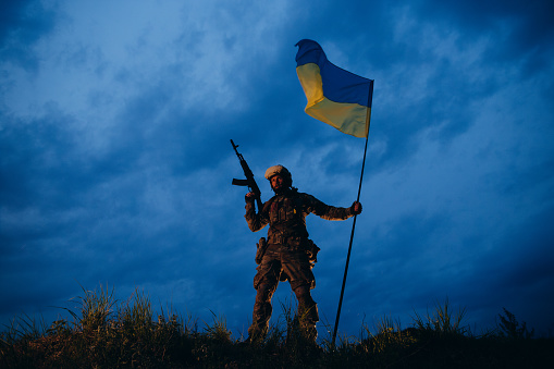 Ukrainian armed soldier is holding a national flag after the battle