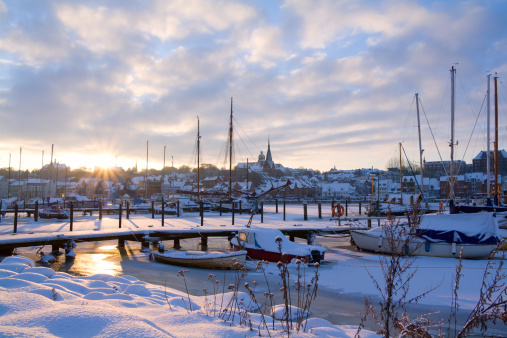 The city of Flensburg in northern Germany at sunset with sailboats in frozen water.