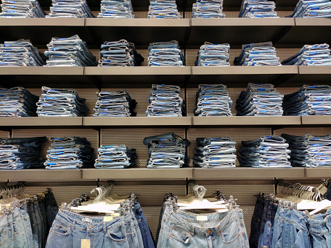 There are stacks of new jeans on the shelves of a clothing store. Clothing retail boutiques
