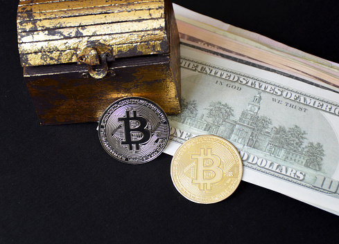 Tiraspol, Moldova - July 24, 2021: bitcoin coin and a chest next to a pack of dollars on a black background. concept of transition to cashless payments and digital money. rejection of paper money. cryptocurrency mining
