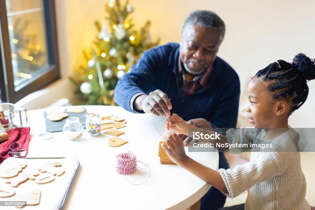 Grandfather and his granddaughter  making gingerbread house Christmas time. Grandfather and his granddaughter joyfully making gingerbread cookies Adult Stock Photo