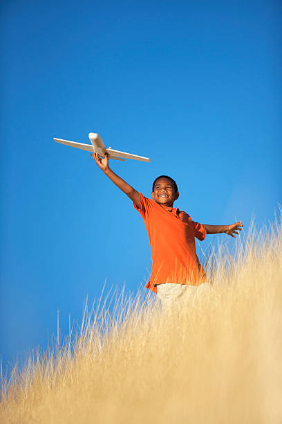 Ethnic Child Playing with Toy Glider Airplane in Field stock photo