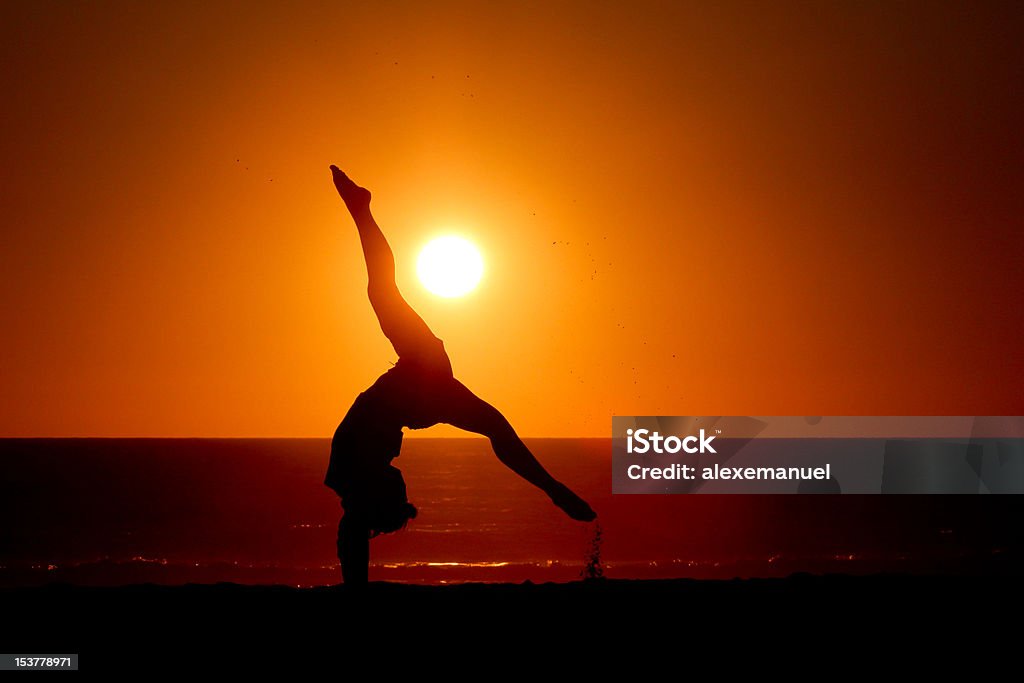 Ginasta menina faz plantar bananeira na praia no pôr-do-sol - Foto de stock de Adolescentes Meninas royalty-free