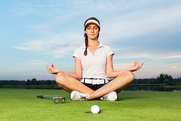 Girl golfer sitting in yoga posture on golf course. Woman golf player sitting on green in yoga posture focusing on ball dropping into cup. golf concentration stock pictures, royalty-free photos & images